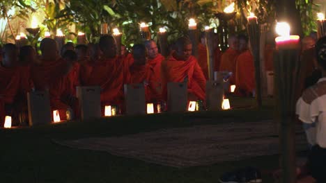 Exterior-Medium-Shot-of-Monks-Sitting-in-Row-With-Cans-of-Drinks-Worshiping-at-Night