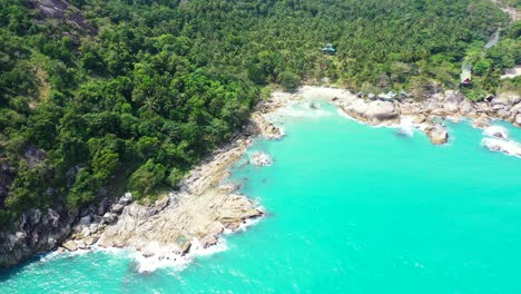 Paradise-tropical-island-with-lush-vegetation-on-hills-and-rocky-coastline-splashed-by-white-waves-of-turquoise-lagoon-in-Thailand