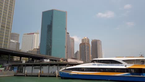 Un-Ferry-Rápido-Blanco-Azul-Yello-Sydney-Estacionado-En-El-Puerto-Con-Edificios-Altos-Rascacielos