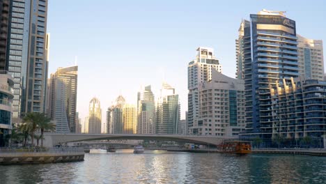 Malerischer-Blick-Auf-Große-Weiße-Yachten,-Die-Bei-Sonnenuntergang-Unter-Der-Kanalbrücke-Von-Dubai-Durch-Hohe,-Moderne,-Schlanke-Wolkenkratzer-Fahren,-Vereinigte-Arabische-Emirate,-Statisch