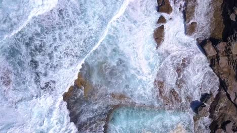 Top-down-bird-eye-view-of-ocean-waves-crashing-strongly-on-to-the-rock-pool-from-the-cliff-in-a-very-windy-day