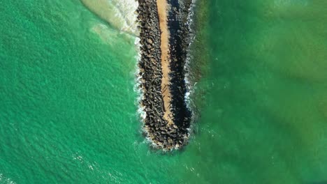 Top-down-drone-shot-of-Southport-seawall,-clear-water-and-surf-crashing,-slow-motion