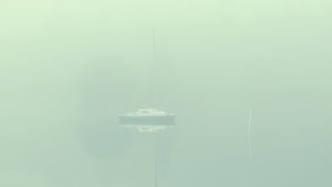 Kleines-Segelboot-Aus-Sperrholz,-Das-Auf-Dem-Dichten-Nebel-Des-Sees-Festgemacht-Ist