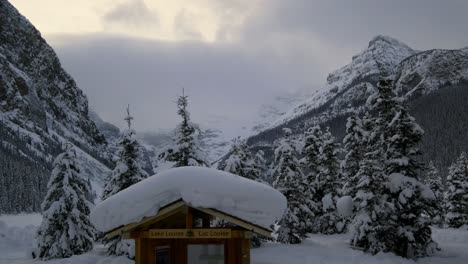 Lake-Louise-Zeichen-Auf-Einer-Holzkonstruktion,-Die-Mit-Dickem-Schnee-Bedeckt-Ist,-Umgeben-Von-Immergrünen-Bäumen-Und-Den-Felsigen-Bergen-Kanadas