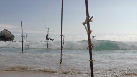 Low-angle,-slow-motion-slide-of-Sri-Lankan-stilt-fisherman-moving-feet-out-of-the-way-of-oncoming-waves