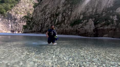 Joven-Caminando-Lentamente-A-Través-De-Un-Río-Poco-Profundo-Con-Agua-Fría-Y-Cristalina-Que-Fluye-Junto-A-La-Montaña-Rocosa