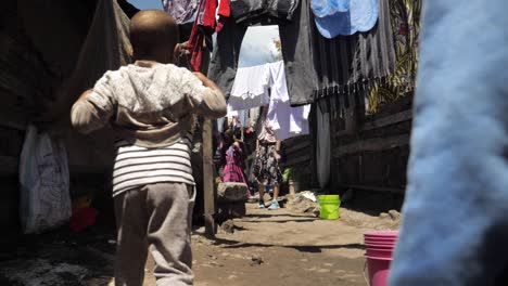 Niños-Africanos-Jóvenes-Caminando-Por-Los-Barrios-Marginales-De-Una-Aldea-Pobre-Mientras-Pasan-La-Ropa---Siguiendo-El-Tiro-De-Seguimiento-180fps-En-Cámara-Lenta