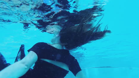 Frau-Im-Schwarzen-Kleid-Schwimmt-Auf-Der-Oberfläche-Des-Blauen-Wassers