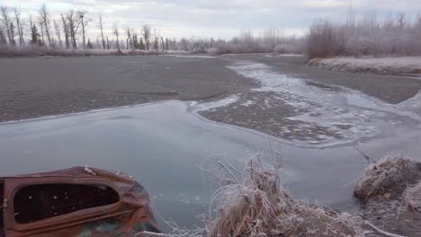 Pan-left-to-reveal-an-old-rusty-abandoned-car-embedded-in-the-ground-on-the-river-bank-of-the-Knik-river-near-Eklutna-Tailrace-area-near-Palmer-Alaska
