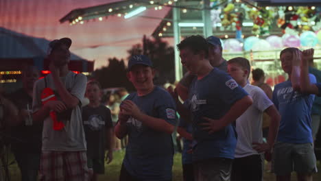 Young-boy-with-friends-playing-speed-pitch-game-at-carnival-at-dusk