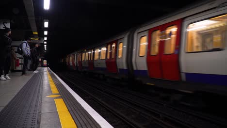 Toma-De-Un-Tren-Que-Pasa-Por-Una-Estación-De-Metro-Llena-De-Gente-Esperando-En-Londres,-Reino-Unido