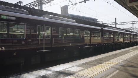 Long-Hankyu-line-train-passing-through-railway-platform-on-a-bright-and-sunny-day,-passengers-on-other-platform-in-the-background