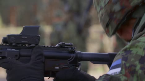 Soldier-aiming-and-firing-rifle-in-a-military-exercise,-soldiers-background,-closeup,-handheld