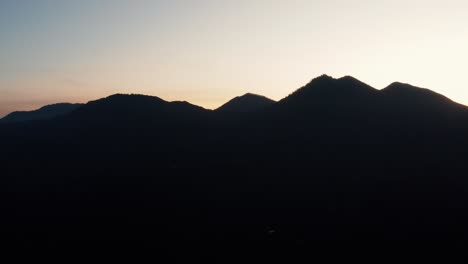 Aerial-drone-view-slowly-approaching-the-silhouette-of-a-mountain-ridge-at-sunrise,-sunset
