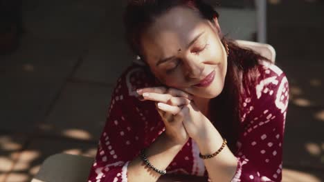 A-close-up-dolly-shot-of-an-attractive-Caucasian-female-seated-outdoors-resting-her-head-on-her-hands,-eyes-closed-relaxing-and-embracing-the-beautiful-moment