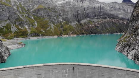 Aerial-view-of-turquoise-waters-of-lake-Limmernsee-and-hydroelectric-dam-in-Linthal-Glarus,-Switzerland-with-cliffs-in-background