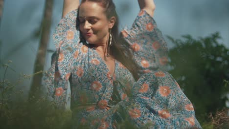 A-hippy-carefree-Caucasian-female-sitting-in-a-grass-field,-arms-outstretched-as-she-dreams-and-appreciates-the-beauty-of-nature-on-a-sunny-day-outdoors