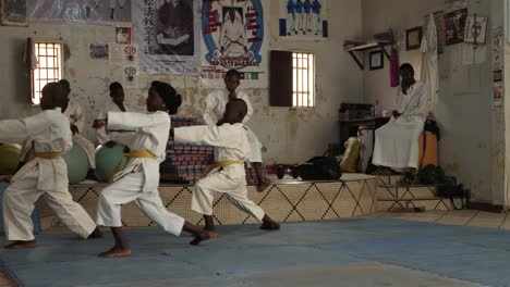 A-shot-of-a-girl-and-two-boys,-wearing-kimonos-with-yellow-belts-train-karate-together-inside-a-karate-school