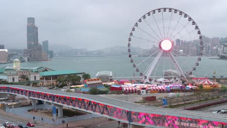 Un-Puente-Peatonal-Está-Decorado-Con-Faroles-Rojos-Chinos-Mientras-La-Gente-Camina-A-Través-De-él-Mientras,-En-El-Fondo,-Hay-Una-Rueda-De-La-Fortuna-En-Hong-Kong