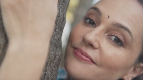 Up-close-of-a-woman-tilting-her-head-and-looking-into-the-camera-while-hugging-a-tree