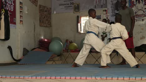 Two-african-kids-train-karate-aside-their-sensei-inside-a-dojo-in-Nouakchott,-Mauritania