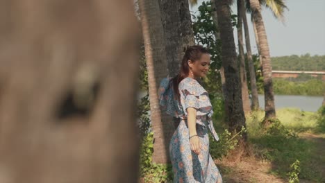 -A-dolly-shot-revealing-an-attractive-carefree-Caucasian-female-dancing-around-the-trunk-of-a-large-palm-tree-on-a-beautiful-day-outdoors,-India