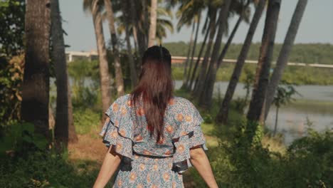 Vista-Trasera-De-Una-Joven-Caminando-Por-Un-Sendero-Forestal-Junto-A-Un-Lago-Con-Un-Vestido-Estampado-Floral