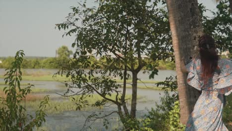 Cheerful-woman-walking-round-a-tree-in-a-forest-by-the-lake