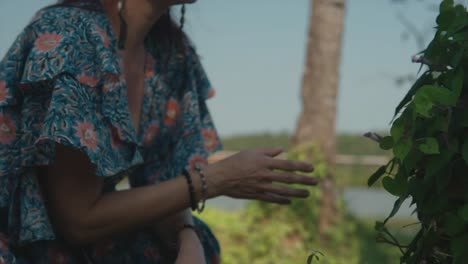 A-close-up-shot-of-a-hand-touching-the-leaves-of-a-plant,-panning-to-reveal-a-carefree-happy-Caucasia-female-smiling-as-she-appreciates-the-beauty-of-nature