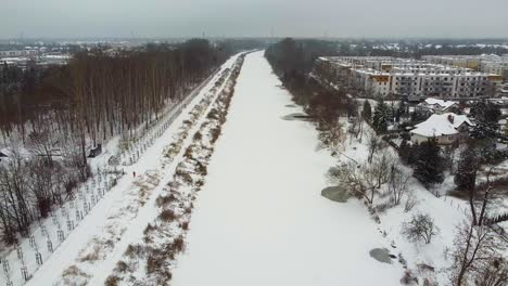 Drone-video-of-frozen-river-next-to-a-forest-covered-in-snow-in-warsaw