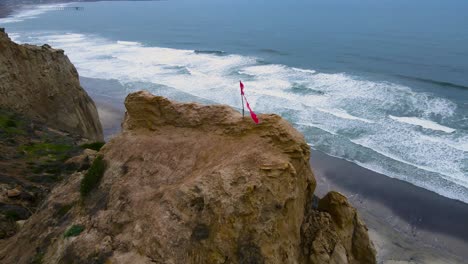 Aerial-view-of-a-torn-red-flag-on-the-bluff-at-blacks-beach-Torrey-pines-California