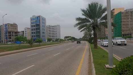 Dolly-Left-Reveal-Of-Traffic-Passing-Along-Highway-Road-Beside-Developments-At-Bahria-Housing-Development-In-Karachi