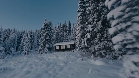 Fpv-flight-between-snowy-mountains-and-trees-arriving-at-wooden-hut-in-winter