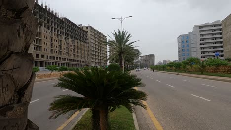 Dolly-Right-Reveal-Past-Tree-Of-Traffic-Passing-Along-Highway-Road-Beside-Developments-At-Bahria-Housing-Development-In-Karachi