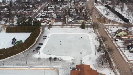Aerial,-people-skating-on-neighborhood-community-ice-rink-during-winter-season
