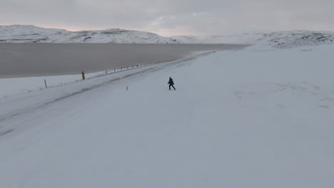 Orbit-view-around-woman-crossing-the-snowy-road-in-countryside,-Iceland