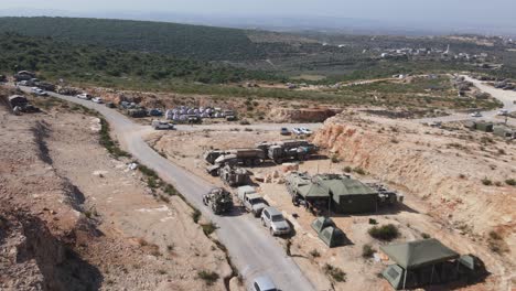 Soldados-Del-Ejército-De-Israel-En-Vehículos-Humvee-Conduciendo-A-Través-De-La-Carretera-Rural-Del-Campo-De-Entrenamiento,-Zona-De-Acampada-Del-Ejército-Israelí,-Toma-Aérea