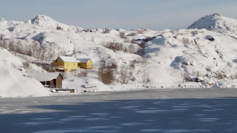 Fixed-shot-of-a-yellow-house-in-the-middle-of-the-icy-mountains-of-Svolvaer-in-Lofoten-islands-close-to-a-frozen-lake