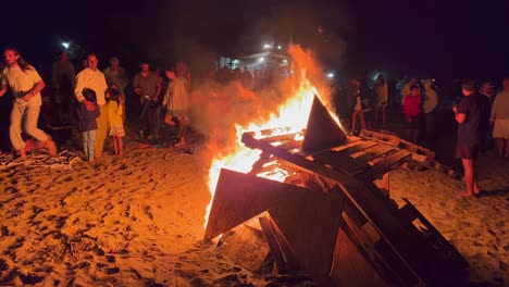 Festival-Tradicional-De-Hogueras-En-La-Playa-En-La-Celebración-De-San-Juan-En-Marbella-España,-Amigos-Y-Familiares-Disfrutando-De-Una-Fiesta-Divertida-Durante-El-Verano,-Gran-Fuego-Ardiente-Y-Llamas-Calientes-Por-La-Noche,-Tiro-De-4k