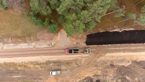 Heavy-digger-taking-black-soil-from-dump-truck,-aerial-top-down-view