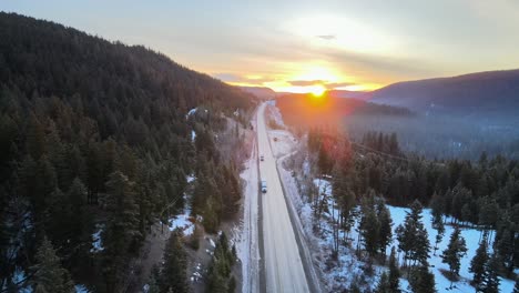 An-Aerial-shot-of-Semi-Trucks-driving-on-Cariboo-Highway-97-During-a-Winter-Sunrise-in-British-Columbia,-Canada
