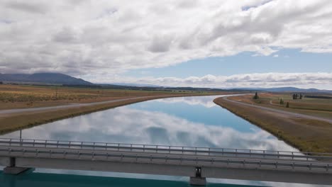 Take-an-unforgettable-journey-as-you-soar-over-the-serene-Pukaki-canals,-with-the-clouds-reflecting-in-the-tranquil-waters