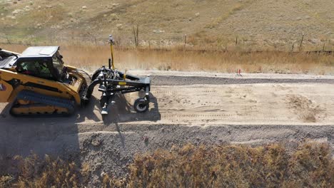 Vista-De-Dron-Del-Cargador-De-Orugas-Compacto-Oruga-Nivelando-La-Superficie-De-La-Carretera-De-Grava