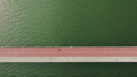 aerial-top-down-of-red-asphalt-bridge-connecting-city-with-pedestrian-cyclist-and-cars-crossing-the-water