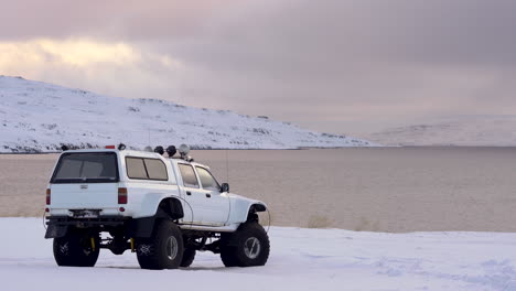 White-super-jeep-overlooking-ocean,-snowy-mountain-background