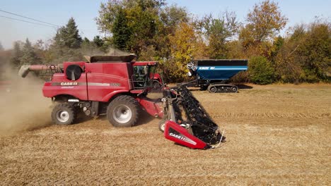 Red-case-8120-harvesting-combine-working-on-wheat-field,-while-case-quadtrac-stands-on-side