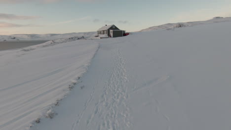 Footprints-in-snow-leading-towards-house-surrounded-by-mountains,