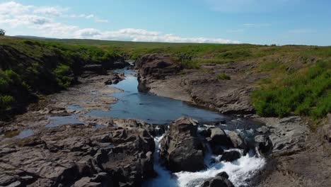 Ascending-drone-shot-showing-idyllic-flowing-river-with-scenic-landscape-in-background-during-sunny-day---Iceland,Europe