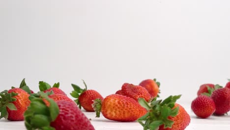 Frische,-Leuchtend-Rote-Erdbeeren,-Die-Herunterfallen-Und-In-Zeitlupe-Auf-Einer-Weißen-Tischplatte-In-Einen-Haufen-Springen