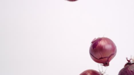 Whole-red-onions-and-skin-raining-down-on-white-backdrop-in-slow-motion